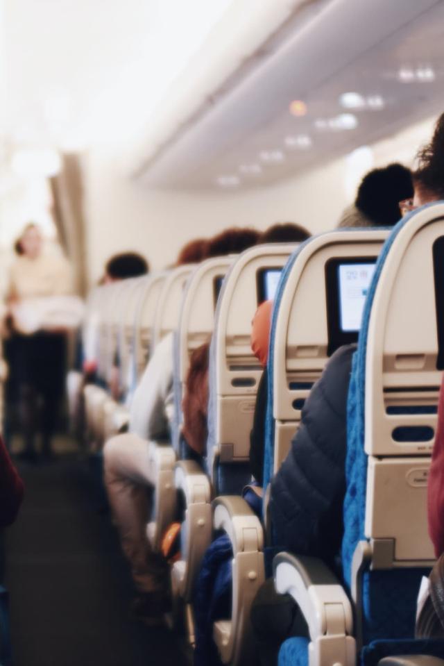 Innenraum eines grossen Passagierflugzeugs mit sitzenden Menschen und einer Stewardess in Uniform, die den Gang entlanggeht