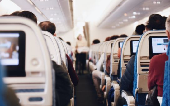 Innenraum eines grossen Passagierflugzeugs mit sitzenden Menschen und einer Stewardess in Uniform, die den Gang entlanggeht