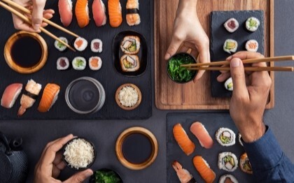 Verschiedene Sushi wie Nigiri, Sashimi und Rollen werden geteilt und mit Stäbchen gegessen